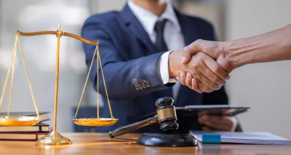 two people shaking hands near a gavel and an office desk
