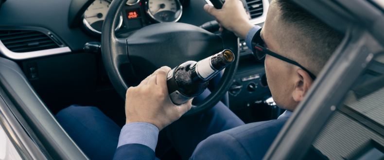 Man holding alcohol bottle while driving