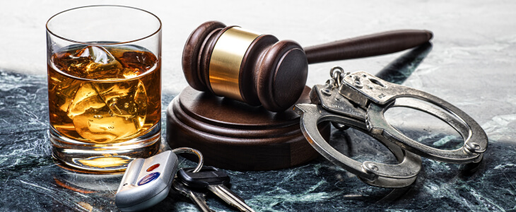 Whiskey glass and gavel with handcuffs illustrating drunk driving