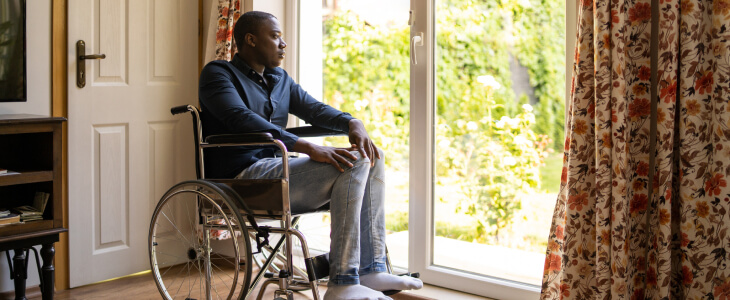 Young man in wheelchair looking sad while staring out back door