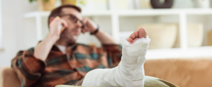 Mature man wearing checkered shirt sitting with broken leg on sofa